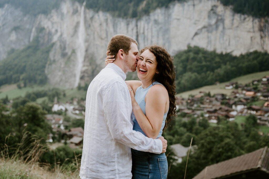 Husband and wife kissing and laughing in Lauterbrunnen with waterfall behind them; How to Elope in Switzerland