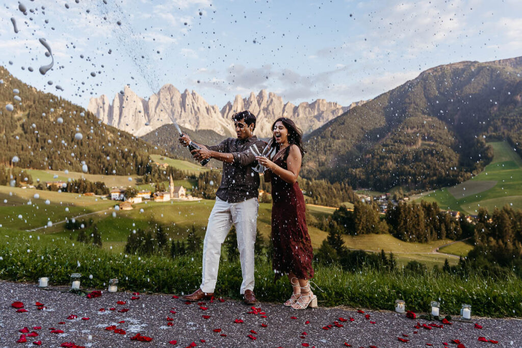 Newly engaged couple pop champagne to celebrate their engagement at Val di Funes