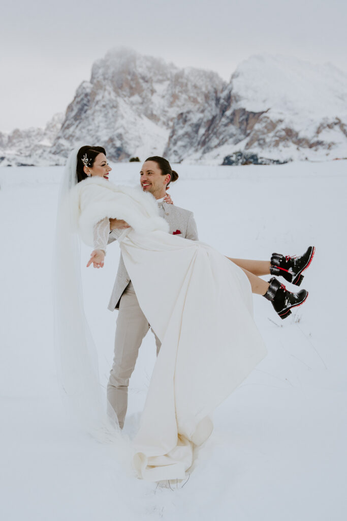 Bride wearing cute fake fur dress during winter elopement, groom is wearing beige suit. They are in the mountains of Alpe di Siusi, the Dolomites