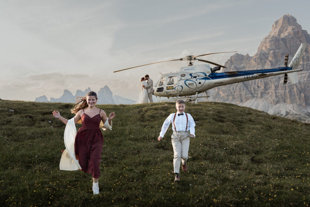 Plan a helicopter elopement with bride, groom, and kids running around with Elikos helicopter service and Tre Cime in the background