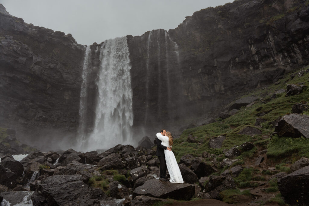 Wide shot of bride and groom standing in front of Fossà on Faroe island