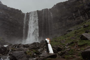 Wide shot of bride and groom standing in front of Fossà on Faroe island