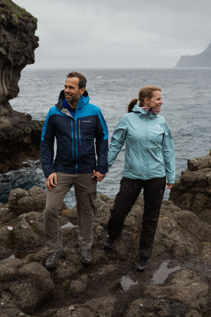 Bride and groom in rain gear embracing the weather on Faroe Islands during their elopement. Learn how to elope on Faroe Islands with Shawna Rae Photography