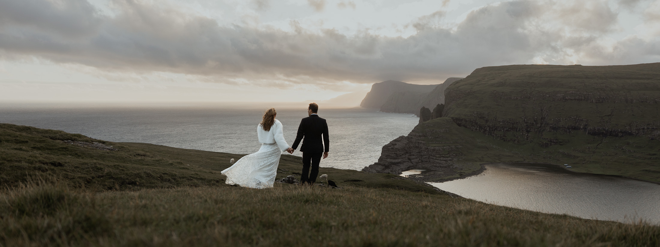 Bride and groom looking at the sunset view on Faroe Islands at Traelanipa with the ocean and lake in view
