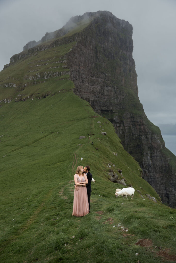 Bride and groom holding each other and kissing with sheep around them at Kallur lighthouse during their elopement