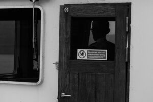 Black and white art portrait of captain holding cigarette out the door of the cabin of his ferry on Faroe Islands