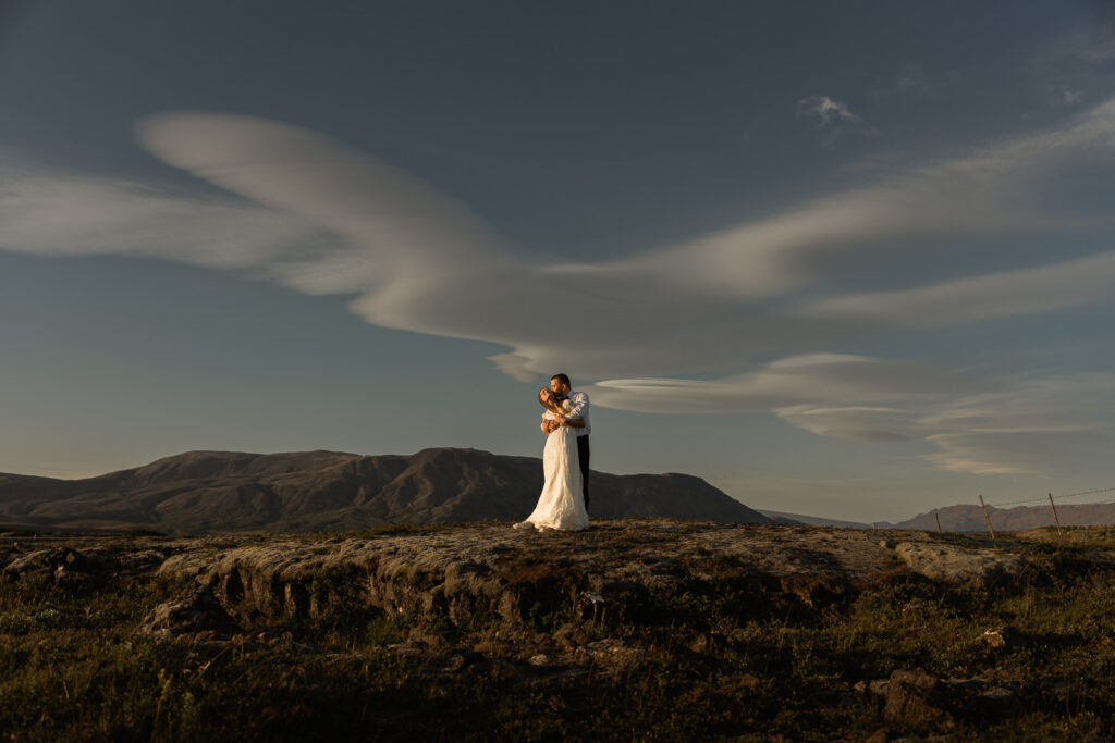 Bride and groom standing with sunny weather and funny clouds in Iceland at Thingvellir National Park during their elopement