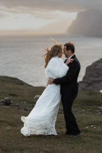 Bride and groom embracing the wind with sunset in the background on Trælanípa, Faroe Islands, for their elopement