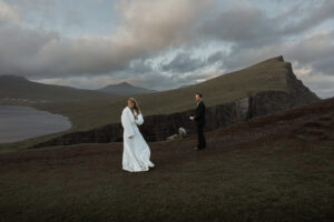 Bride and groom laughing as a sheep takes their vow renewal spot on Trælanípa on Faroe Islands