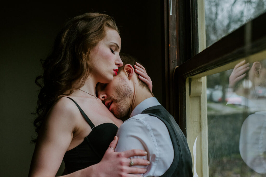Woman and man by a window in their couples boudoir outfits