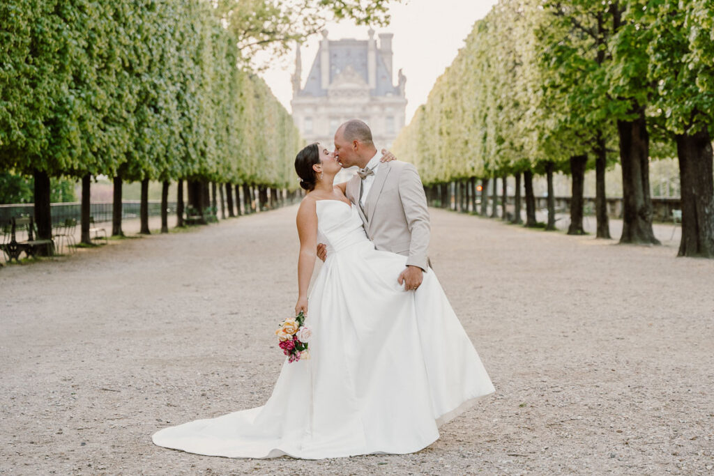 Bride and groom kissing and leaning with parallel trees at Tuileries Gardins; How to Elope in Paris