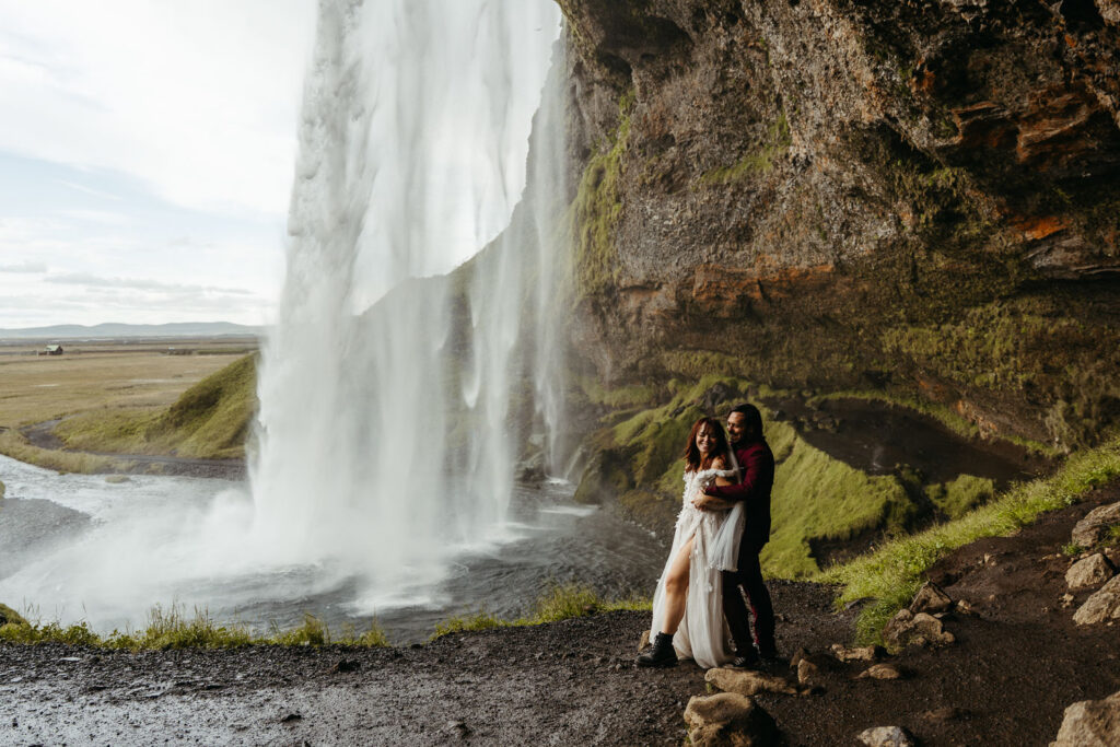 Bride and groom holding each other with Seljalandfoss. Best places to elope in Iceland