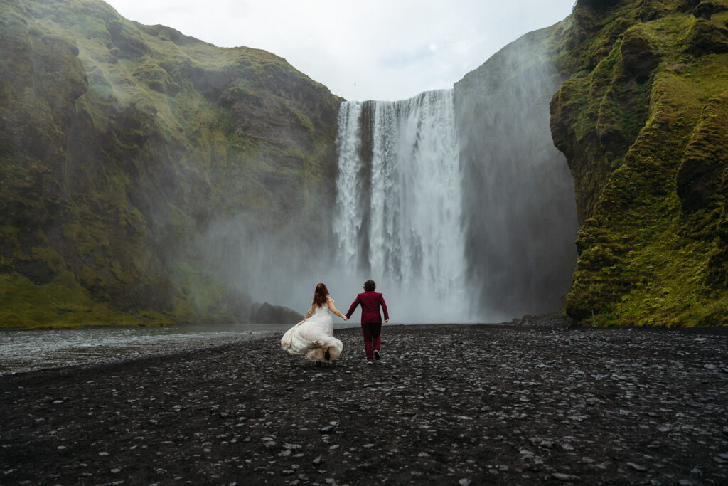 Bride and groom running towards Skogafoss; How to Elope in Iceland