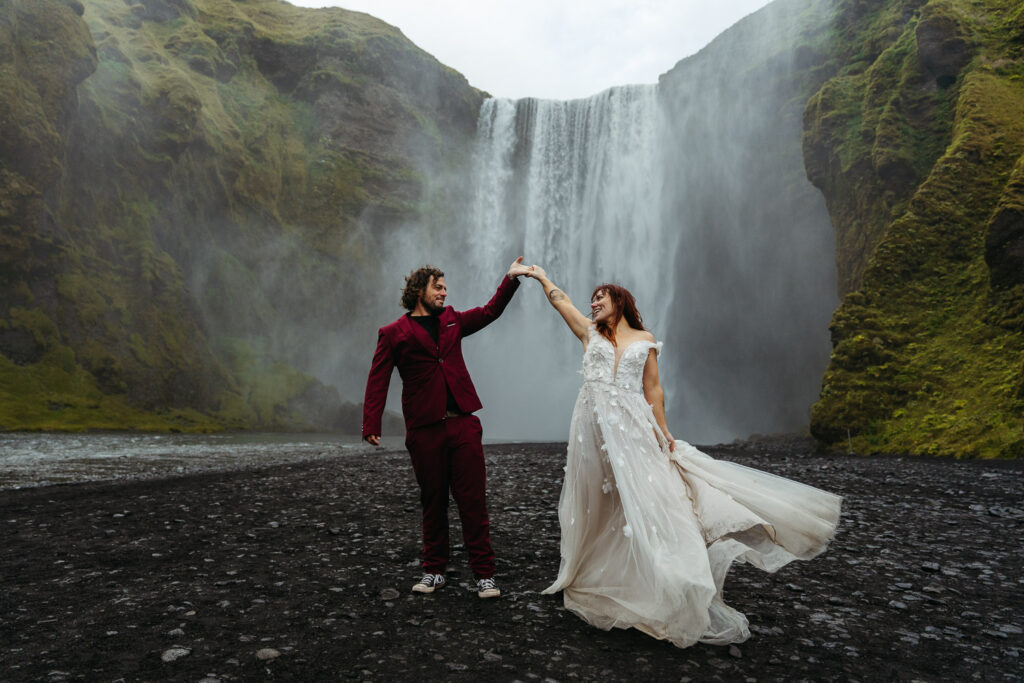 Bride and groom holding hands with Skogafoss behind them. Best places to elope in Iceland